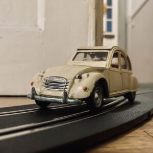 Ein altes Spielzeugauto eines Ciroen 2CV (Ente) auf des Schiene einer Carrera Rennbahn