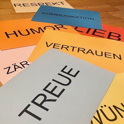 Verschiedene bunte Karten mit Schlagworten zu Werten in einer Beziehung liegen auf dem Boden. Oben eine Karte mit dem Aufdruck Treue.